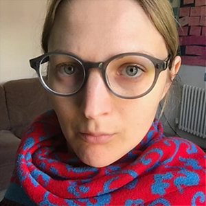 Editor Alice Powell, wearing round glasses and a red-and-blue patterned scarf, indoors.