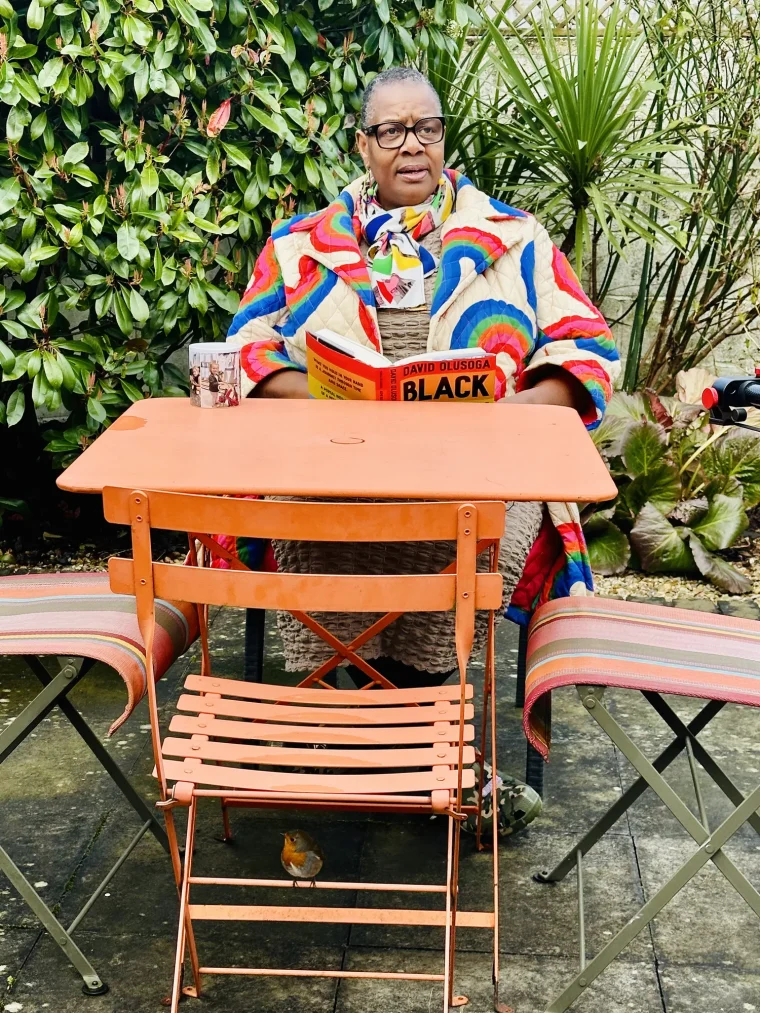 Kemi at an orange garden table in a colourful jacket, holding David Olusoga's book 'Black and British', in Farming: Kemi's Story.