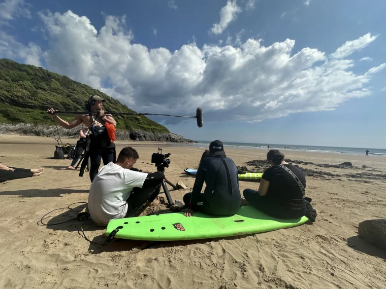 Crew filming a surfer interview on the beach with a boom mic and camera, behind the scenes on Everything Is Waves.