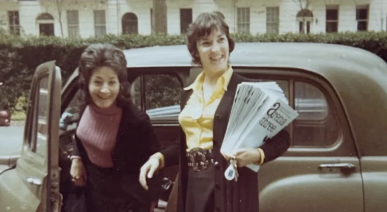 Vintage photo of two women beside a classic car, one holding copies of the lesbian magazine Arena Three, from the documentary Jackie.