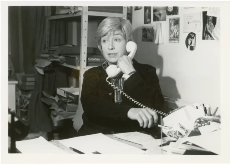 Jackie Forster on the telephone at a busy desk in her office, in a still from the documentary Jackie.