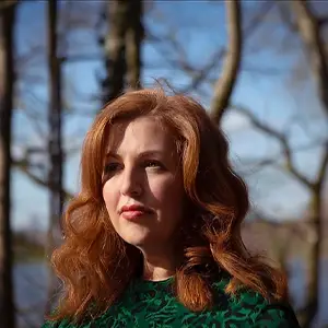 Filmmaker Jeanie Finlay, with long auburn hair and a green top, photographed outdoors.