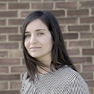 Filmmaker Waad Al-Kateab, with long dark hair and a striped top, against a brick wall.